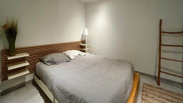 A modern bedroom with a wooden headboard, a bedside table with a lamp, a ladder, and a patterned bedspread. - BEL AIR - 3-bedroom house with a garden (Mimizan)