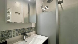A modern bathroom with a white sink, a mirror, a shower with a handheld showerhead, and a tiled backsplash. - BEL AIR - 3-bedroom house with a garden (Mimizan)