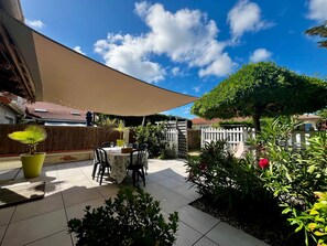 Ein Patio mit Tisch und Stühlen, einem großen Sonnenschirm und verschiedenen Pflanzen.