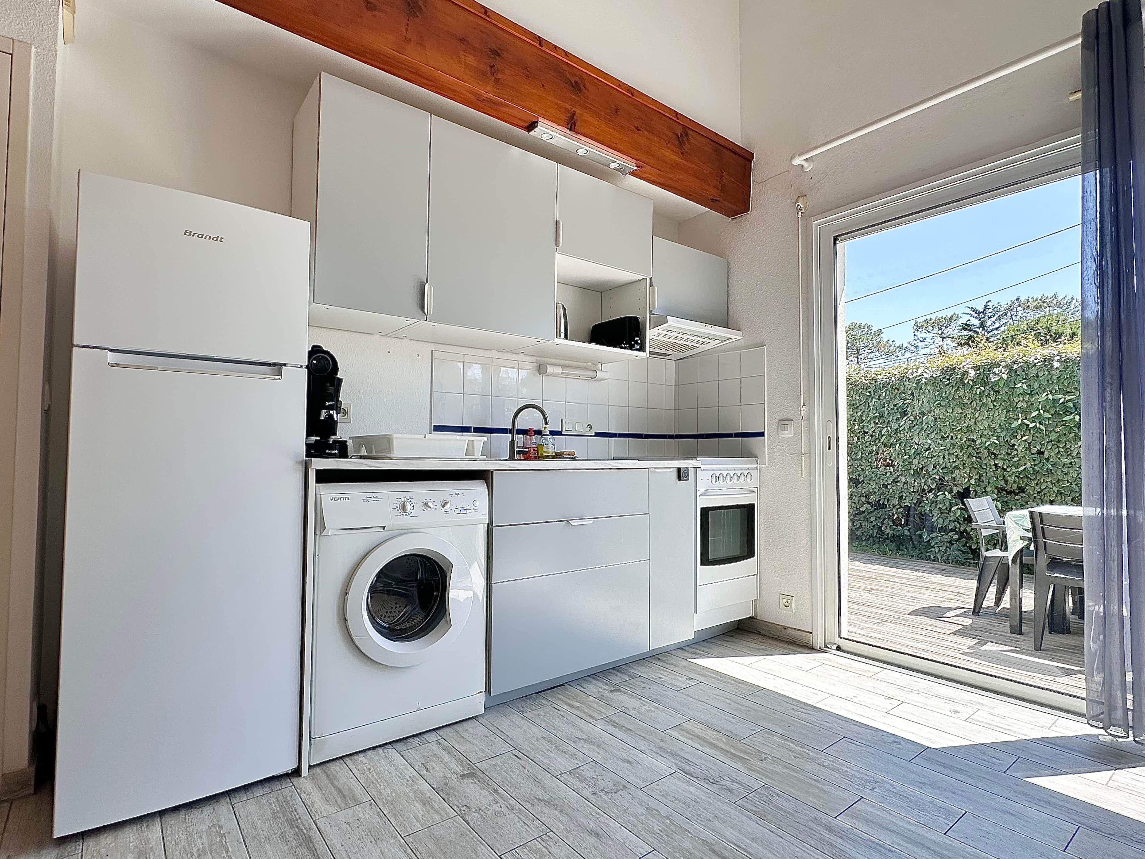 A compact kitchen with a washing machine, oven, and a dining area with a view of greenery.