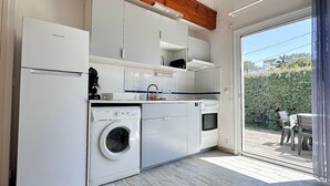 A compact kitchen with a washing machine, oven, and a dining area with a view of greenery. - Fronton 5 - 2-bedroom ground-floor apartment, 900 meters from the ocean (Mimizan)