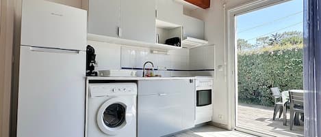 A compact kitchen with a washing machine, oven, and a dining area with a view of greenery.