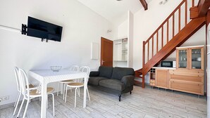 A compact living space with a dining table, chairs, a sofa, a staircase, and built-in cabinets. - Fronton 5 - 2-bedroom ground-floor apartment, 900 meters from the ocean (Mimizan)