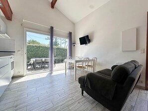 Ein Zimmer mit Esstisch, Stühlen, einer Couch, einem an der Wand montierten Fernseher und einer Küchenzeile.