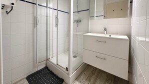 A modern bathroom with a glass shower enclosure, a white sink with a mirror, and a tiled floor. - Fronton 5 - 2-bedroom ground-floor apartment, 900 meters from the ocean (Mimizan)