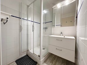 Ein modernes Badezimmer mit Duschkabine aus Glas, einem weißen Waschbecken mit Spiegel und Fliesenboden.