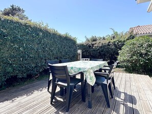An outdoor wooden deck with a table and chairs, surrounded by dense foliage. - Fronton 5 - 2-bedroom ground-floor apartment, 900 meters from the ocean (Mimizan)