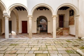 Ein Innenhof mit Bögen, einem Schachbrettmuster-Boden und einer Treppe.