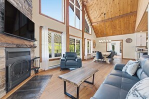 A spacious living area with a fireplace, leather sofa, dining table, and large windows. - Spa & pool Access - Refuge au fil des saisons (Mont-Blanc)