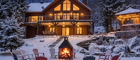 Una cabaña con chimenea, mobiliario exterior y un paisaje nevado.
