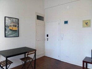 Quarto com uma mesa preta, uma cadeira de madeira, uma porta branca e um quadro na parede.