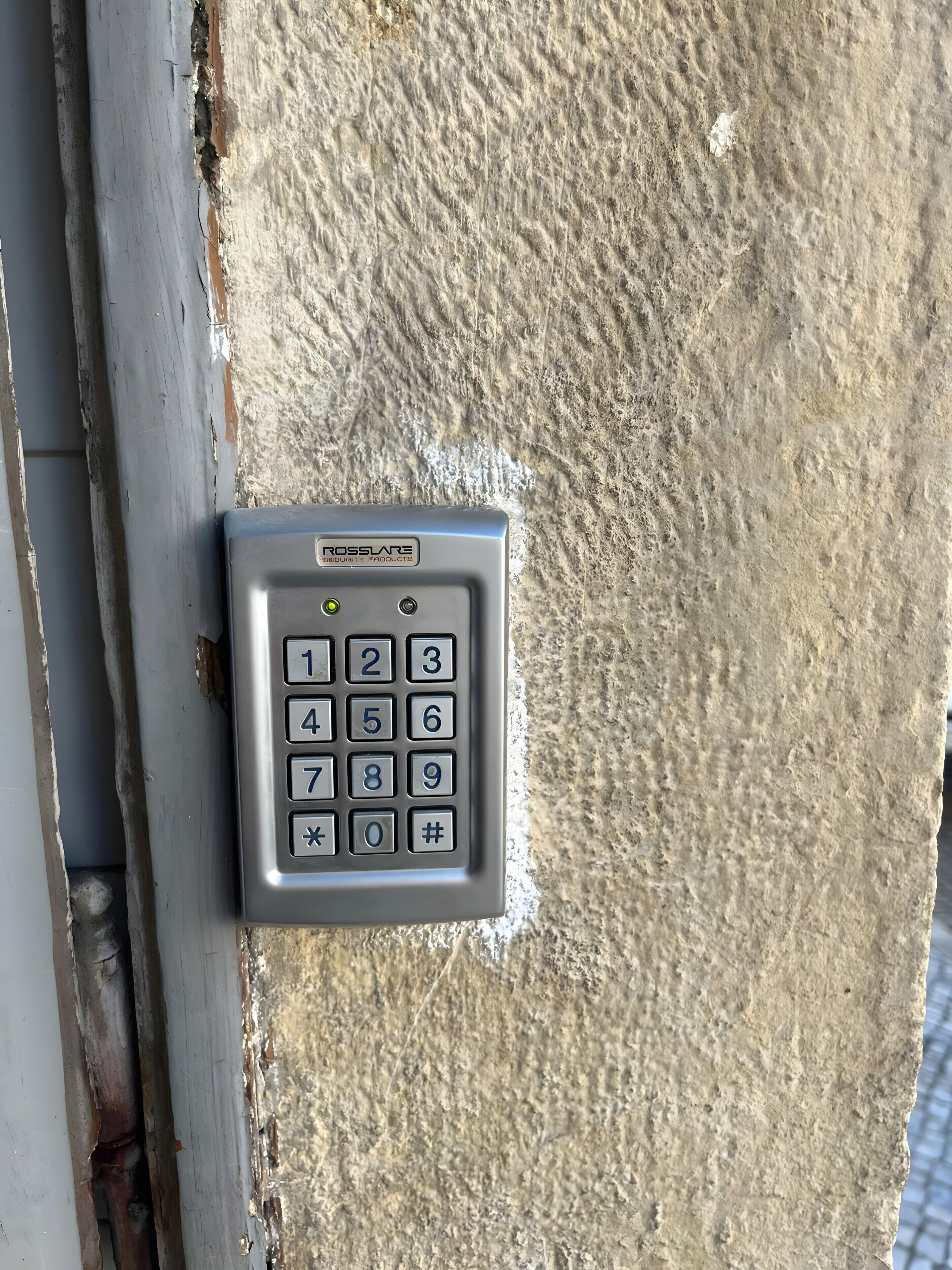 A security keypad mounted on a textured wall, with numbers 0-9 and symbols for * and #.