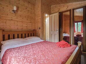 Ein Schlafzimmer in einer Holzhütte mit einem Bett, einem Nachttisch und einer Tür zu einem anderen Raum.