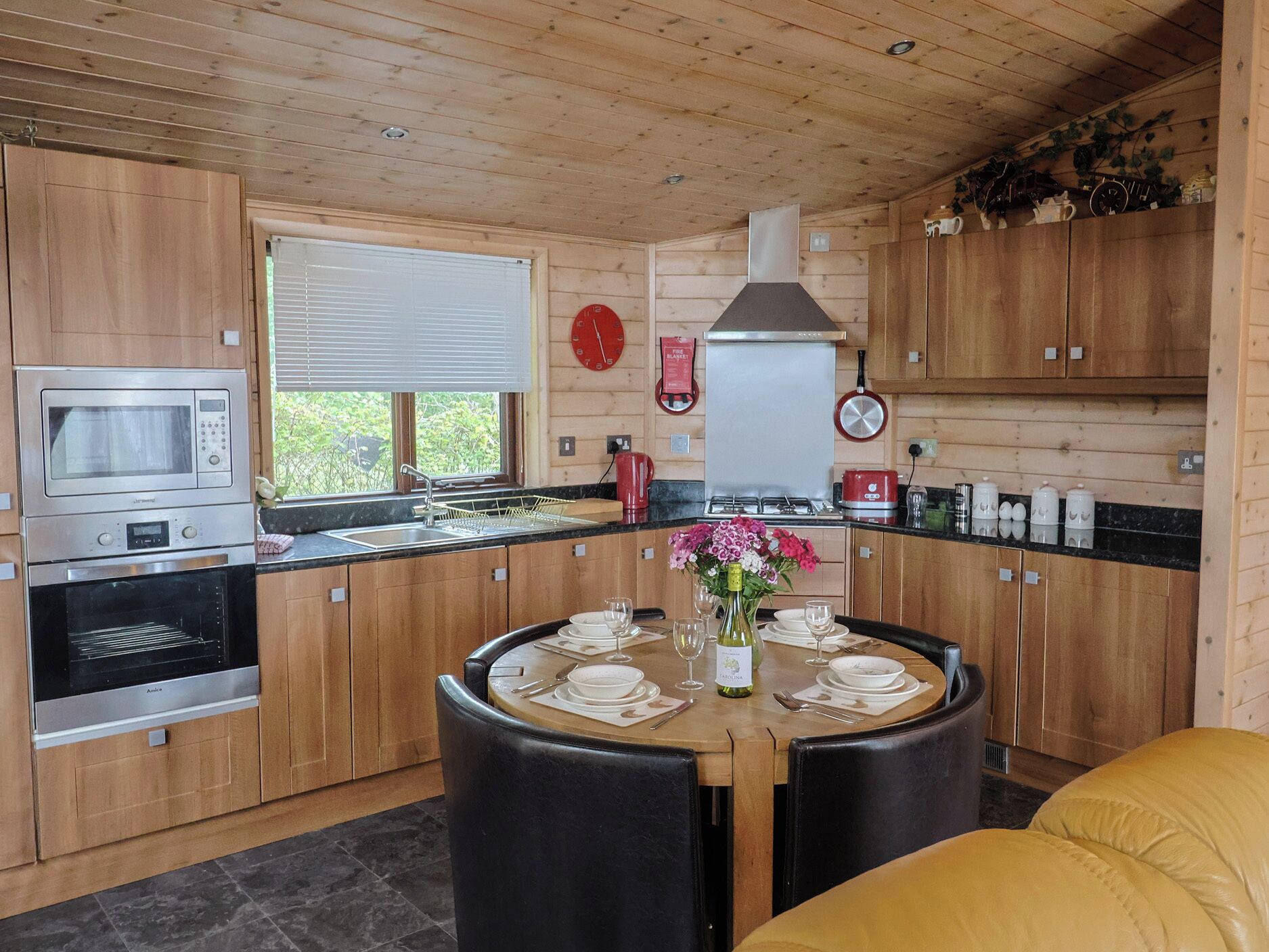 Een moderne keuken met houten kastjes, een inbouwoven, een magnetron, en een eethoek met een ronde tafel voor vier personen.