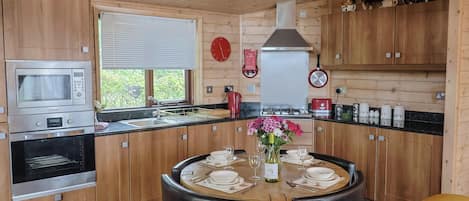 Una cocina moderna con armarios de madera, horno empotrado, microondas y comedor con una mesa redonda para cuatro comensales.