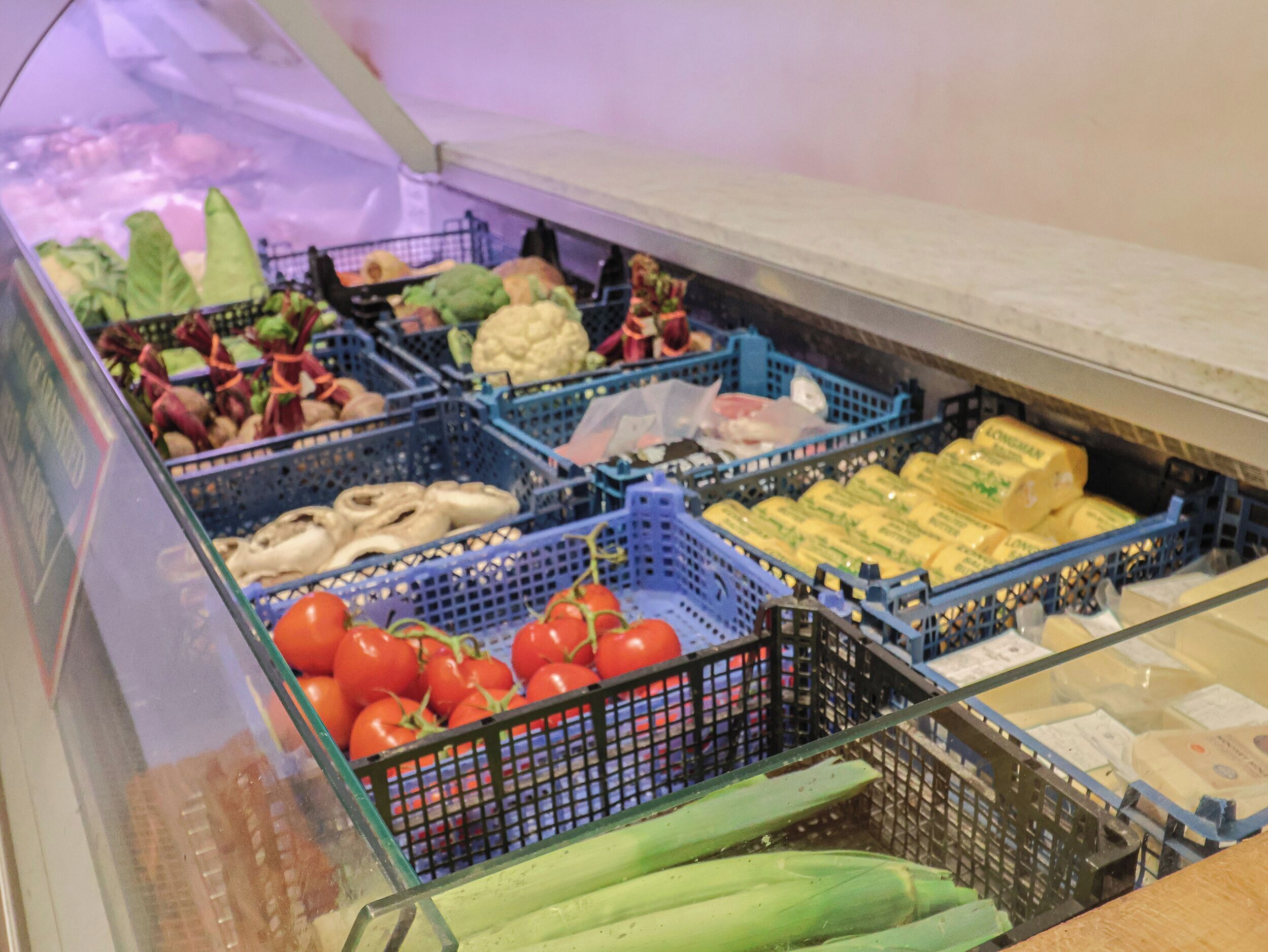 Exposição de vários vegetais e produtos lácteos em uma seção refrigerada de um supermercado.