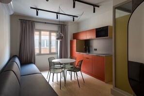 Ein kompakter Wohnbereich mit Sofa, Esstisch, Stühlen, einer Küchenzeile und einem großen Fenster.