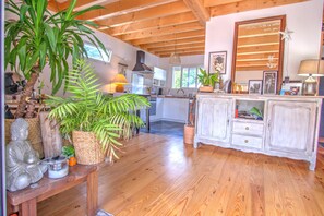 A spacious kitchen with wooden beams, a dining area with a bench, and a white cabinet with drawers. - Chalet Cottage Charming Gite in Arcachon Bay (Gujan-Mestras)