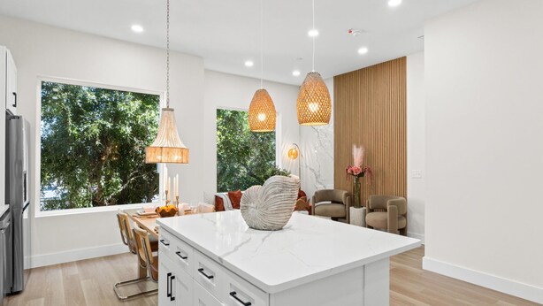Cozinha moderna com armários brancos, bancada de mármore e luminárias pendentes.