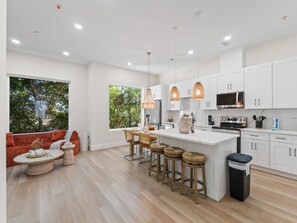 Una cocina moderna con armarios blancos, una isla central, taburetes de bar y una zona de comedor con un sofá rojo.