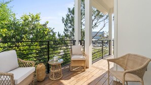 Um deck de madeira com móveis de vime, uma mesa de vidro e vista para o horizonte urbano.
