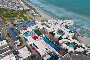 Vue aérienne d’une zone résidentielle côtière, avec des bâtiments, une plage et une route.