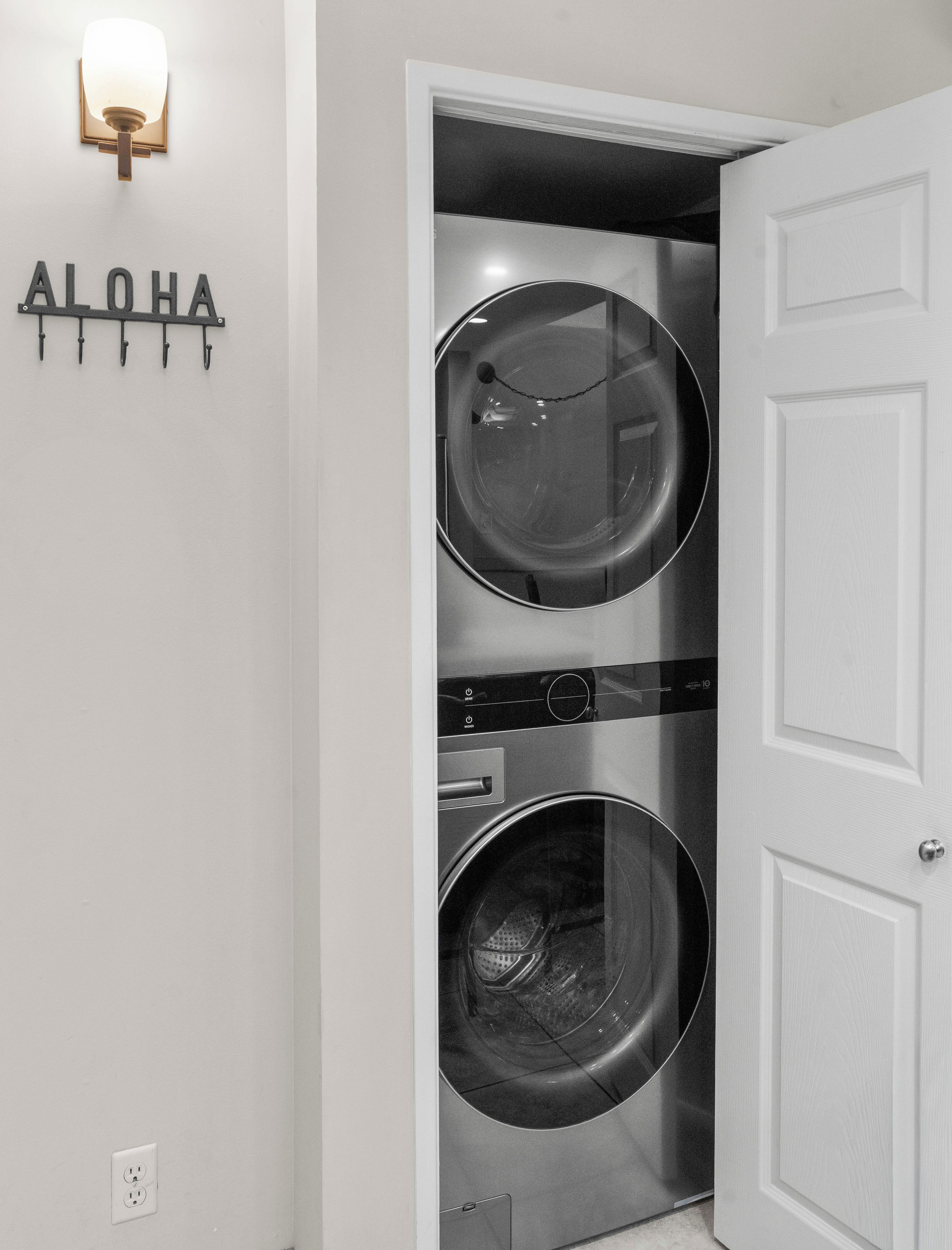 A laundry room with two stacked front-loading washing machines, a wall-mounted light fixture, and a door with a simple design.