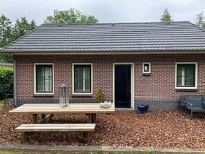 Een gebouw van baksteen met een pannendak, een bankje en een kleine tafel met een schaal.