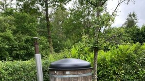 A cylindrical outdoor structure with a chimney, surrounded by grass and trees. - Eendje 2 | Luxe recreatiewoning met hottub (Ermelo)