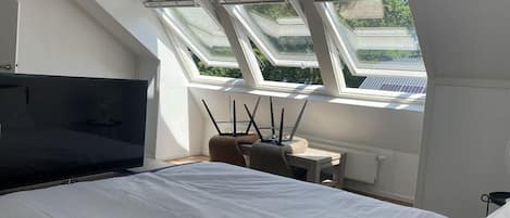 Un dormitorio con cama, escritorio y silla. Hay tragaluces sobre la cama.
