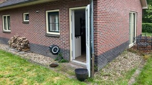 A brick house with a door open, a garden, and a wheelbarrow. - Eendje 2 | Luxe recreatiewoning met hottub (Ermelo)