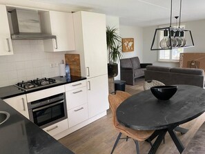 Een moderne keuken met witte kasten, een gasfornuis en een oven. Er is een eethoek met een ronde tafel en stoelen.