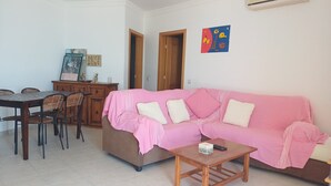 Una sala de estar con un sofá rosa, una mesa de comedor de madera con sillas y una pequeña mesa de centro de madera.