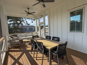 A covered outdoor deck with a wooden table and chairs, a sofa, and a ceiling fan.