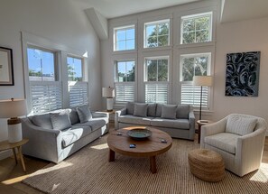 A spacious living room with a high ceiling, large windows, and a modern design.