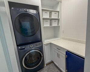 A laundry room with a front-loading washer and dryer, white storage baskets, and a countertop.