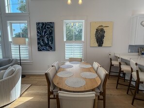 A dining area with a round table, six chairs, and two windows with blinds.