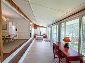 A spacious room with a wooden floor, a dining area with chairs, a table, and a window with a view of the outdoors. - DC56: Silver Queen| Centrally Located | New Decks (Ocracoke)