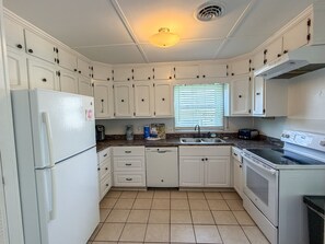 A kitchen with white cabinets, a refrigerator, a dishwasher, a sink, and a stove. - DC56: Silver Queen| Centrally Located | New Decks (Ocracoke)