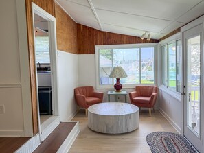 A room with a wooden ceiling, two chairs, a round table, and a window with a view of the outside. - DC56: Silver Queen| Centrally Located | New Decks (Ocracoke)