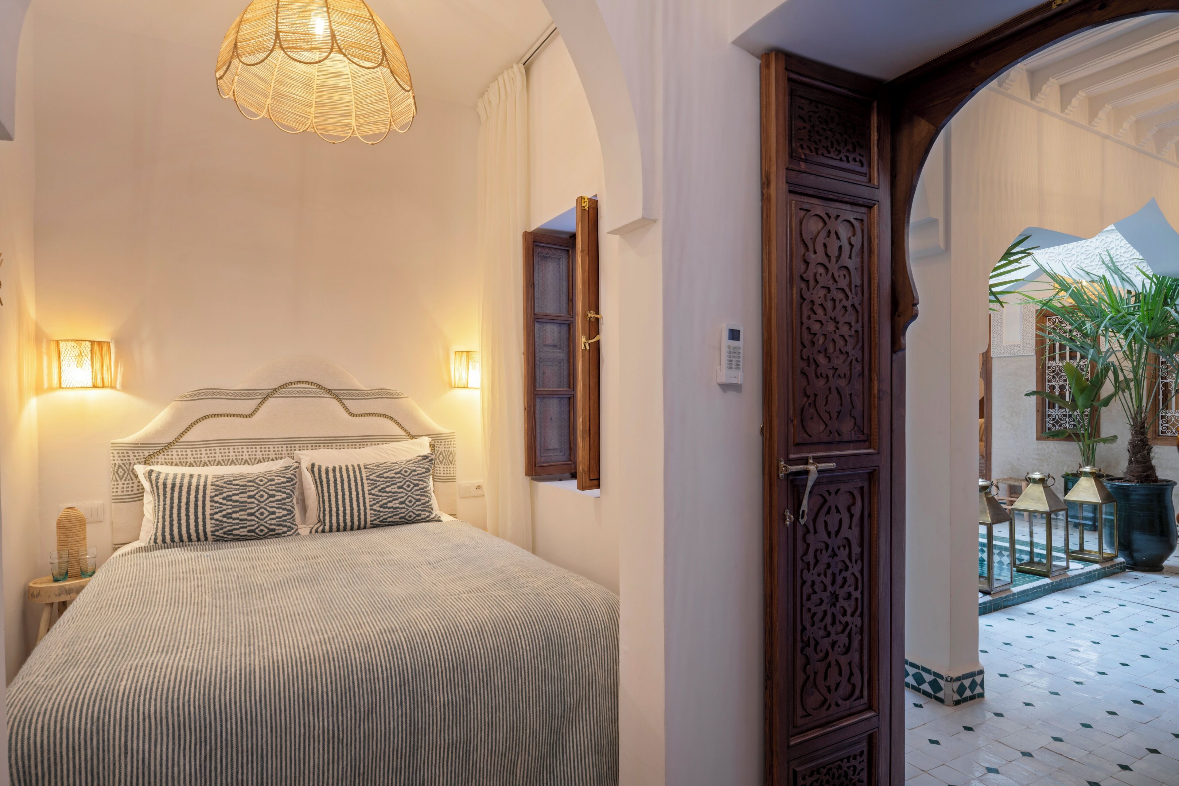 A bedroom with a bed, bedside lamps, and a door leading to a courtyard with potted plants.