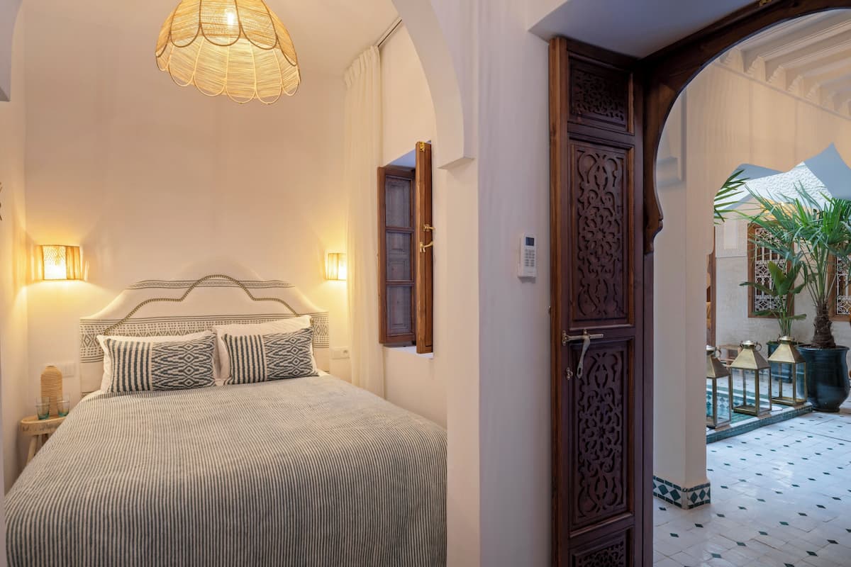 A bedroom with a bed, bedside lamps, and a door leading to a courtyard with potted plants.