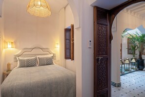 A bedroom with a bed, bedside lamps, and a door leading to a courtyard with potted plants. - Bab Akoul Medina & spa (Marrakech)