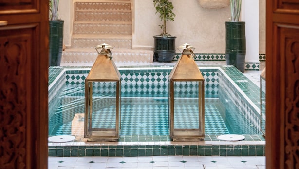 An indoor swimming pool with a tiled floor, surrounded by wooden arches and potted plants. - Bab Akoul Medina & spa (Marrakech)