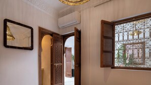 A room with a bed, an open door leading to a hallway, a wall-mounted air conditioner, and a window with decorative iron bars. - Bab Akoul Medina & spa (Marrakech)