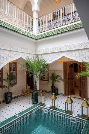 Interior com vários níveis, piscina, plantas em vasos e grades ornamentais.