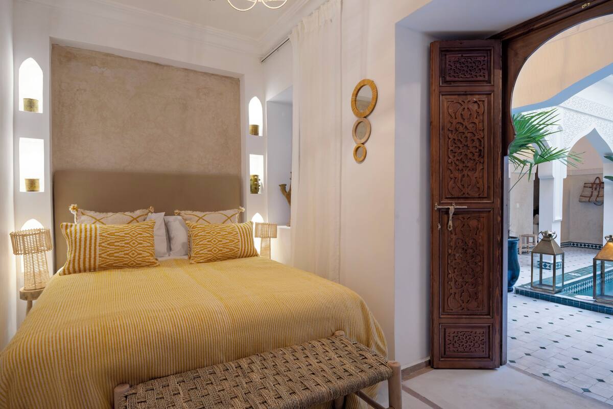 A bedroom with a bed, bedside lamps, a bench, and a decorative door.
