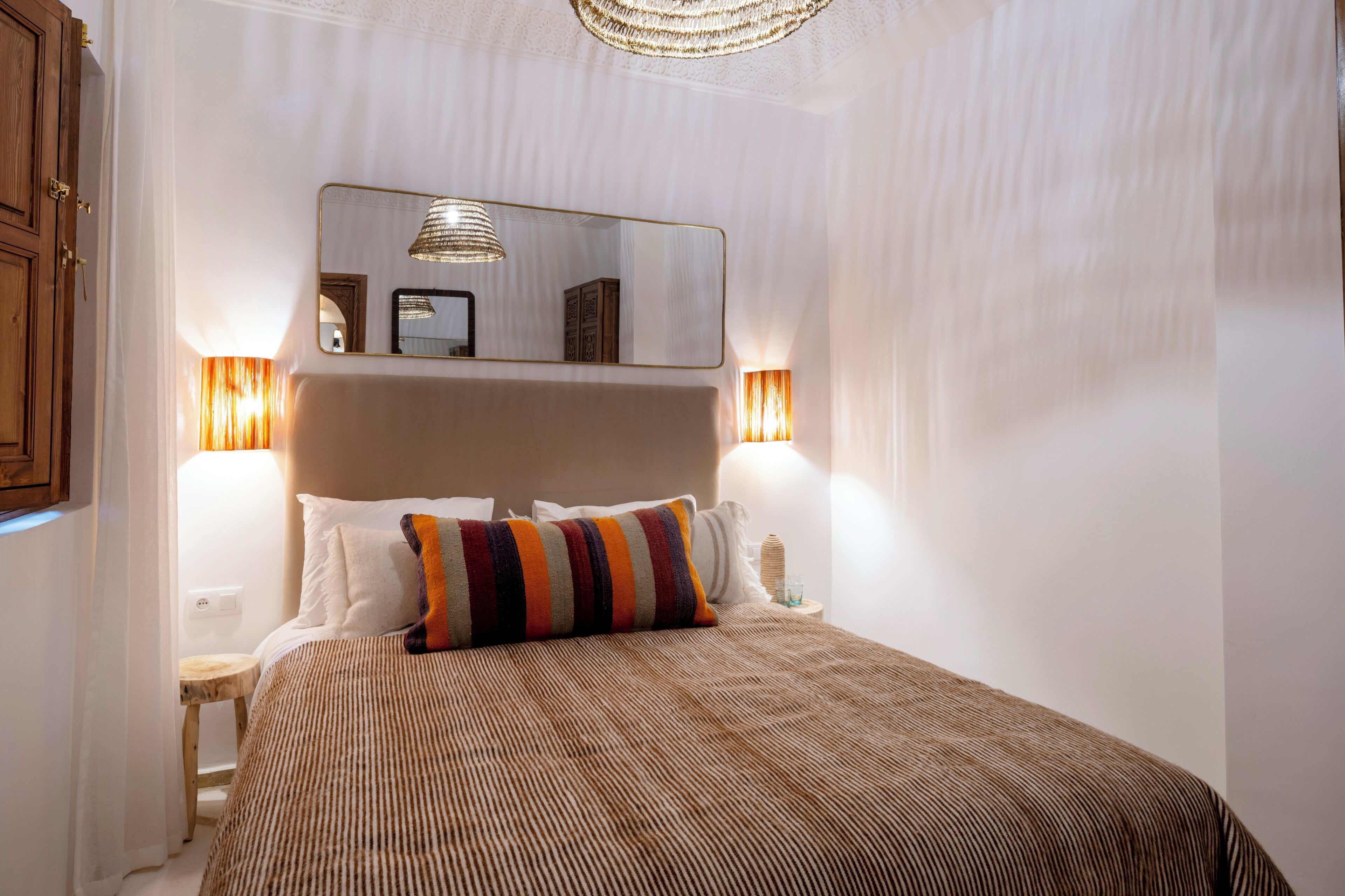 A neatly made bed with a striped bedspread, a mirror above it, and two bedside lamps.