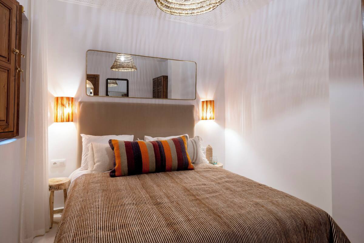 A neatly made bed with a striped bedspread, a mirror above it, and two bedside lamps.