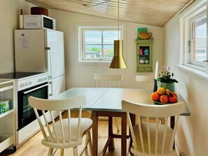 Une cuisine avec des appareils électroménagers blancs, une table à manger, des chaises, une fenêtre et une vue sur l’extérieur.